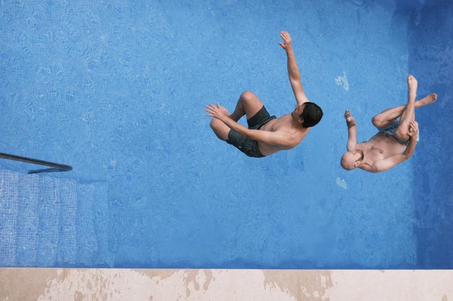 a photograph of two men are swimming in a pool with their hands up