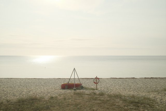a photograph of a man standing on a beach next to a red boat
