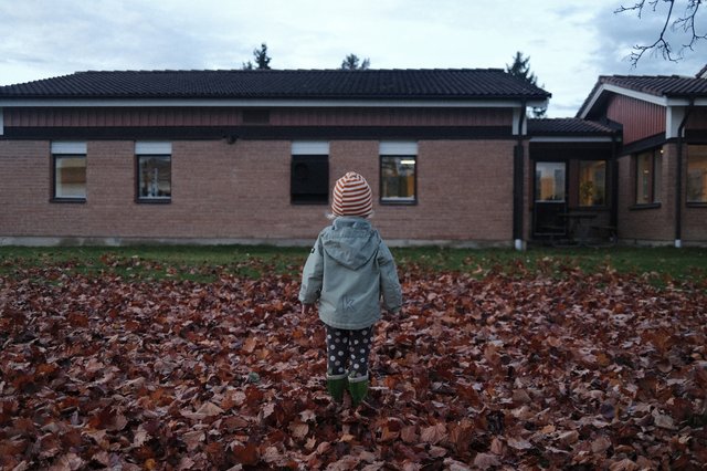 a photograph of a child standing in front of a house with a hat on