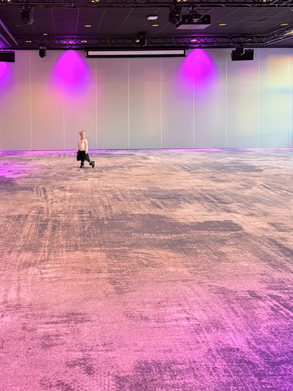 Person standing on a lit indoor dance floor under purple stage lights.