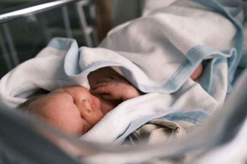 Newborn baby rests in a light blue and white blanket, face turned to the side.
