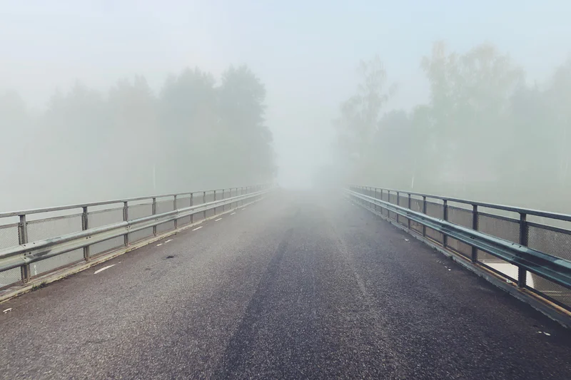 Road stretching ahead into dense fog, with metal guardrails on both sides.