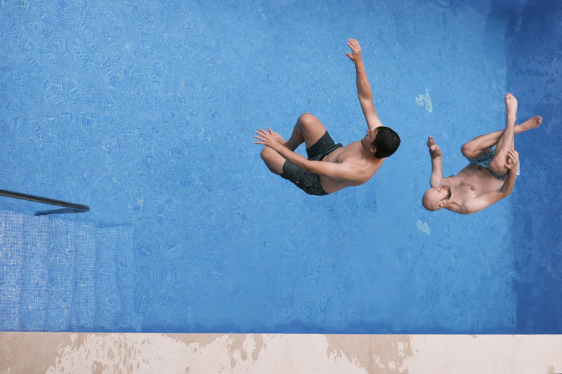 Two people are mid-dive into a blue pool with water splashes around them.