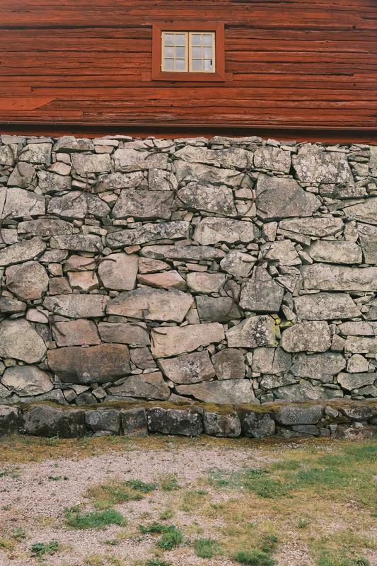 Wooden wall above a stacked stone retaining wall with a small rectangular window in the upper section.