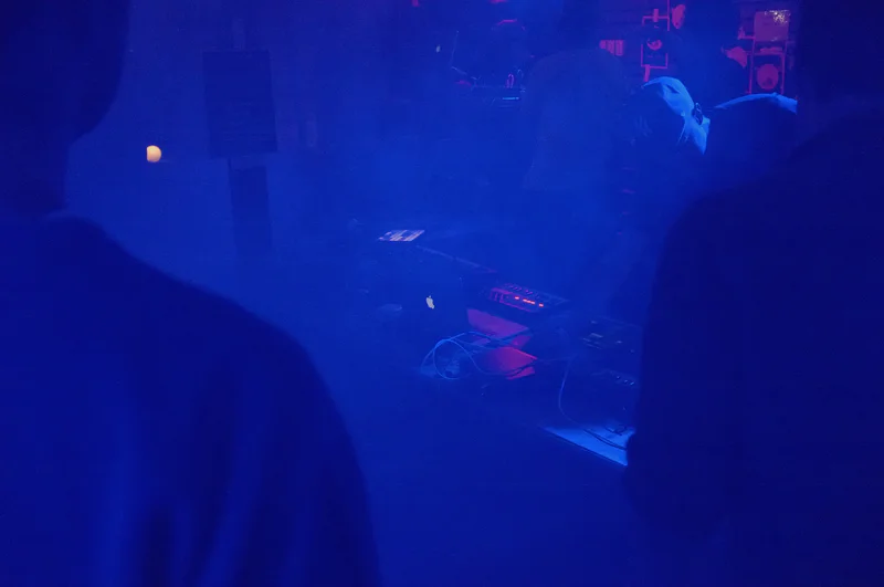 Blue-lit stage with a person near a mixing console and cables in a dark club.