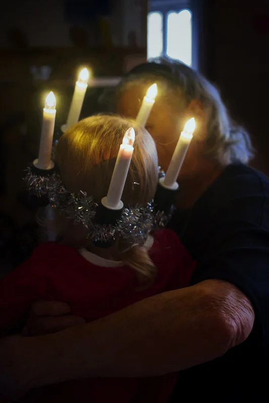 Two people in warm candlelight kiss a child in front of four lit candles on a menorah.