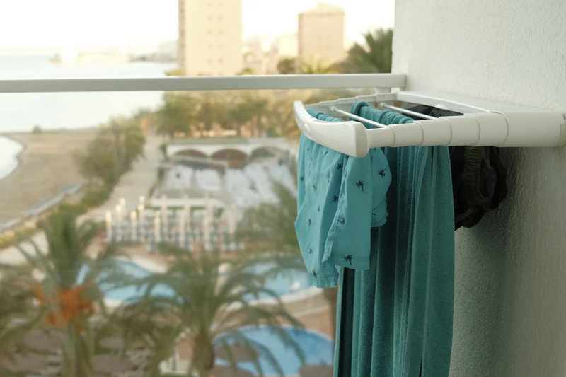 Swimsuits and a towel hanging on a hotel balcony railing near a pool view.