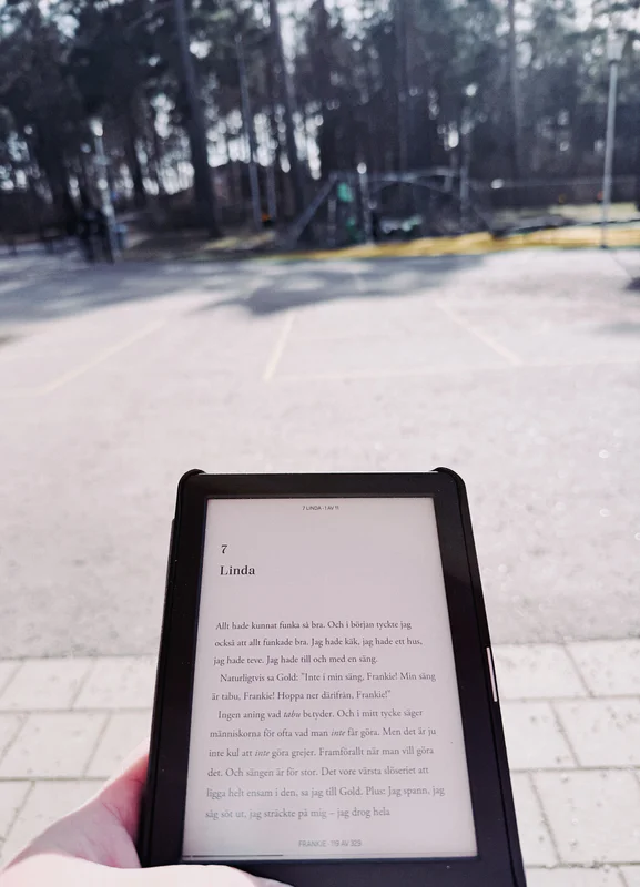 Hand holding a tablet showing Swedish text in the screen outdoors on a paved path.