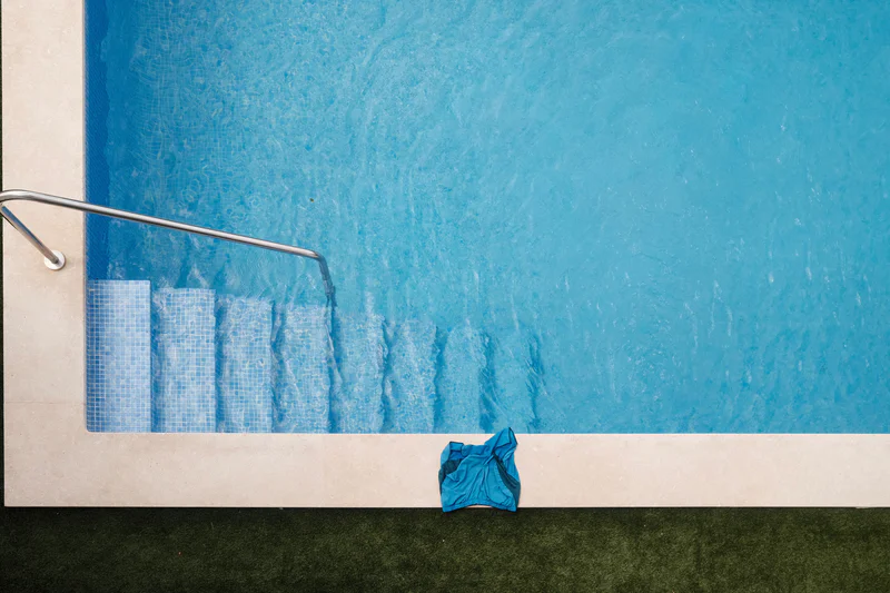 Blue tiled pool wall with metal handrail, white ledge, and a crumpled blue cloth on the floor