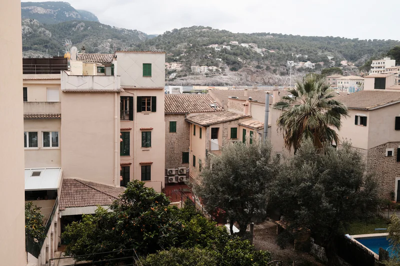 View of hillside town buildings, rooftops, trees, and a small pool in the foreground.