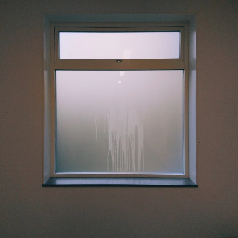 Square window with white frosted glass in a beige wall, framed by light-colored trim.