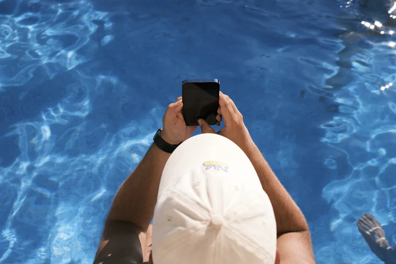 Person in a pool holding a smartphone above the water, seen from behind.