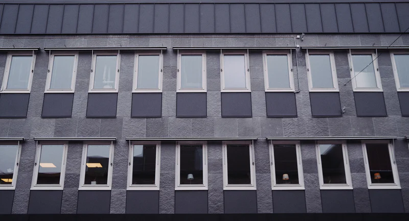 Facade of a multi-story office building with rows of rectangular windows and dark awnings.