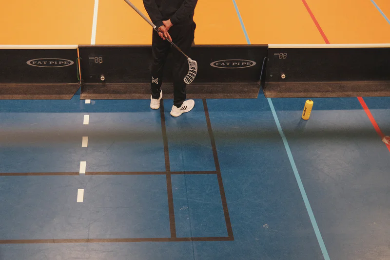 Floorball player holding a stick on a blue indoor court near floor boundary markers.