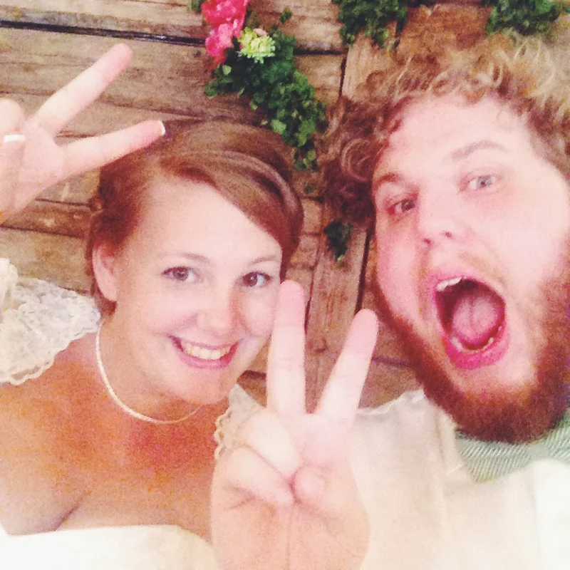 Smiling couple taking a close-up selfie, making peace signs in an indoor barn setting.