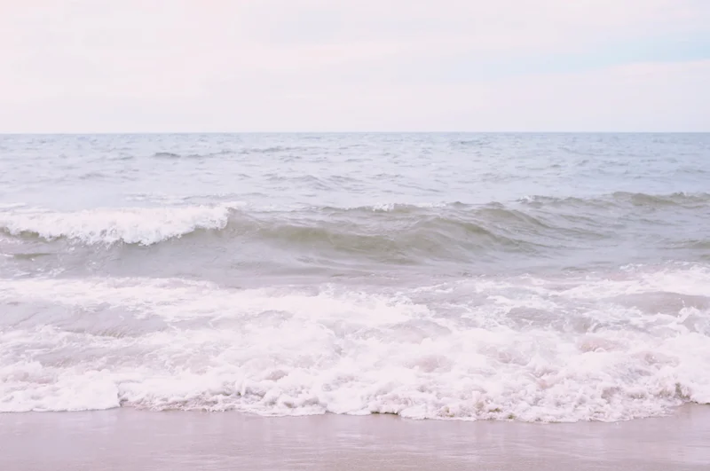 Waves roll onto a sandy beach under a pale, overcast sky.