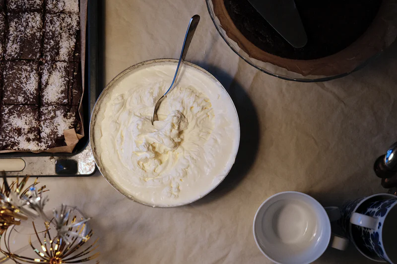 Top view of a bowl of whipped cream with a spoon, surrounded by a tray, candles, and coffee cups.