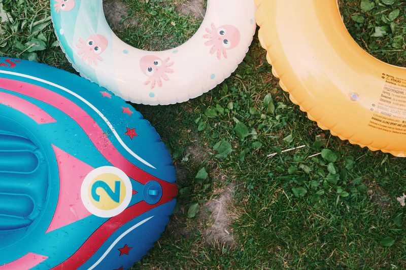 Colorful inflatable pool toys on grass, including pink-and-blue rings with star and octopus designs.