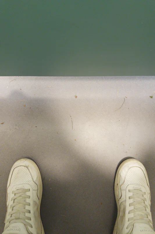 Bottom view of two white sneakers on a scuffed bathroom stall floor.