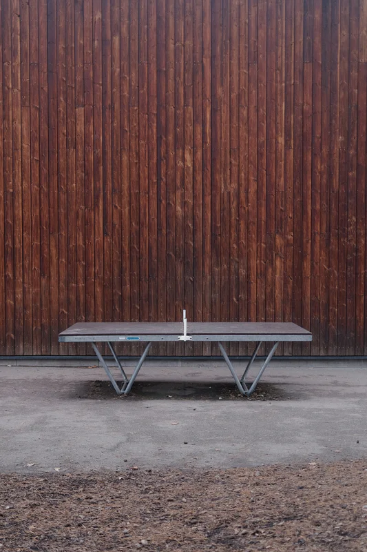 Outdoor ping pong table on concrete ground in front of a wooden fence.