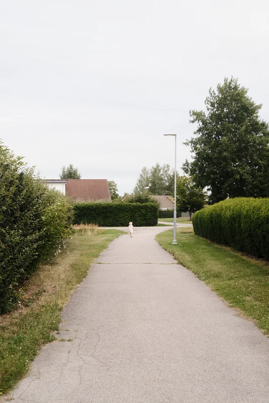 A young child walks along a paved path between neatly trimmed hedges.