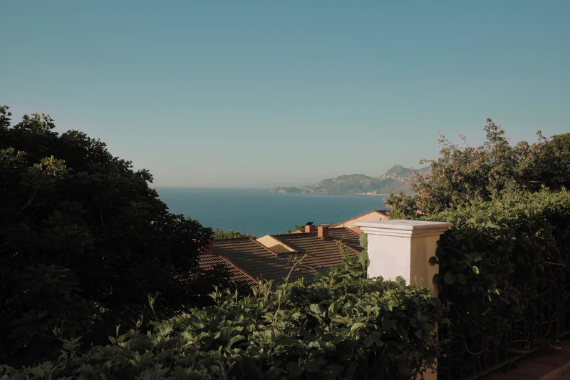 View over rooftops toward a calm bay and distant mountains under a clear blue sky.