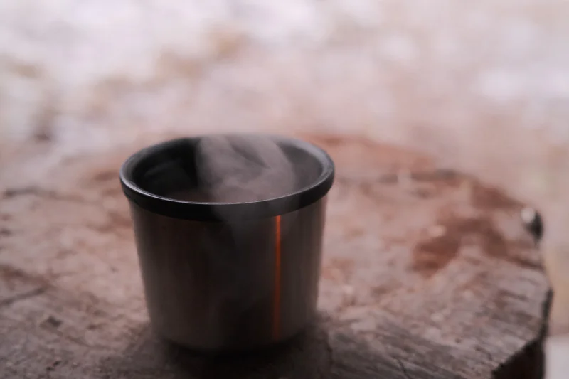 Black metal cup with a dark interior resting on a weathered wooden surface outdoors.