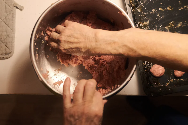 Hands crumble minced meat into a metal pot, with a black pan nearby.