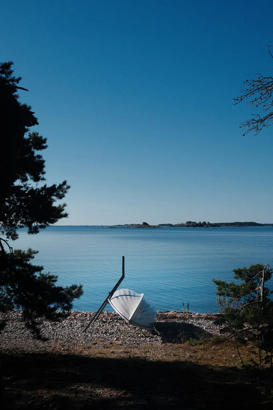 A white boat is beached near the shore beside a calm blue sea under a clear sky.