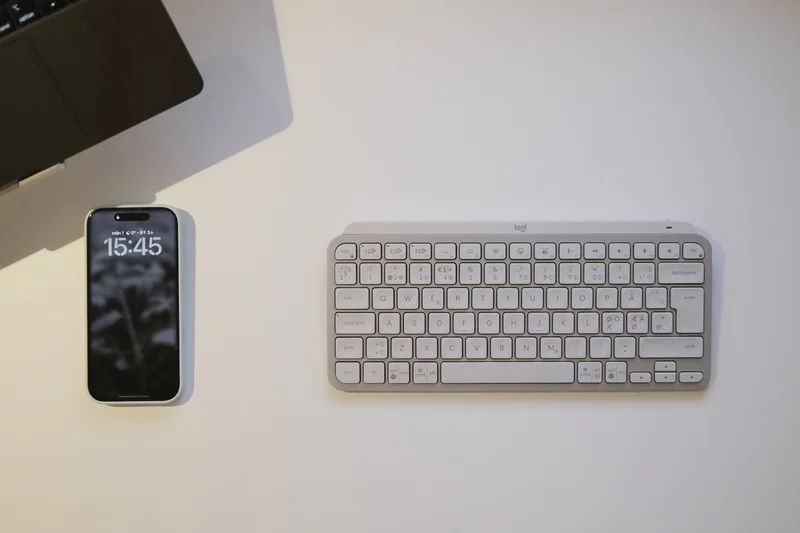 Smartphone displaying 15:45 and a compact keyboard on a white desk.
