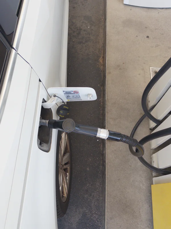 White diesel pump nozzle and hose beside a fuel dispenser on a concrete floor.