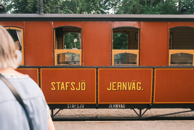 Orange railroad passenger car with windows and gold letters reading “STAFFSJÖ JERNVÄG.”