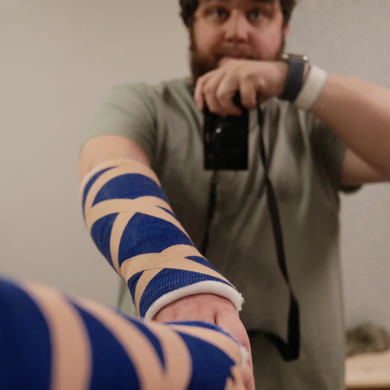 Person with blue-and-white striped arm cast leaning forward and pointing camera.