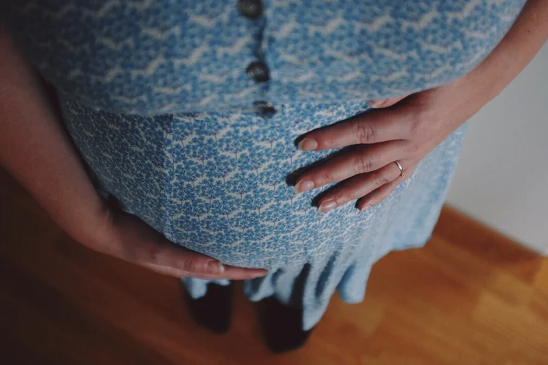 Person in a blue patterned dress holding their belly with both hands.