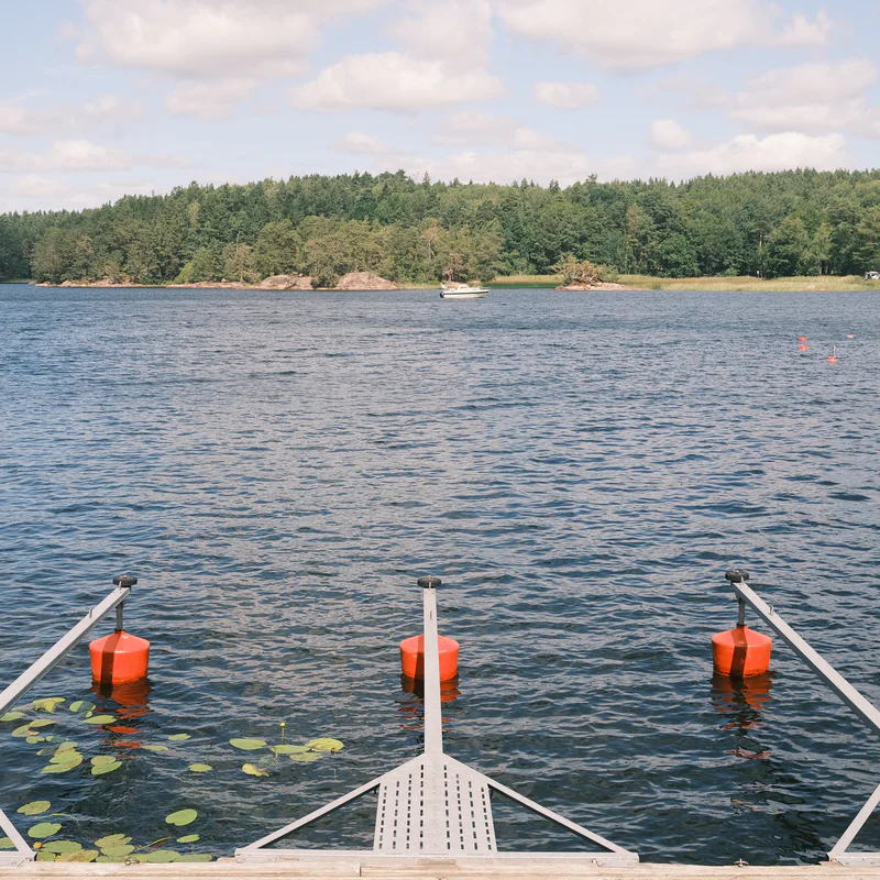 Lake view from a dock with orange buoys and lily pads in calm water under a cloudy sky.