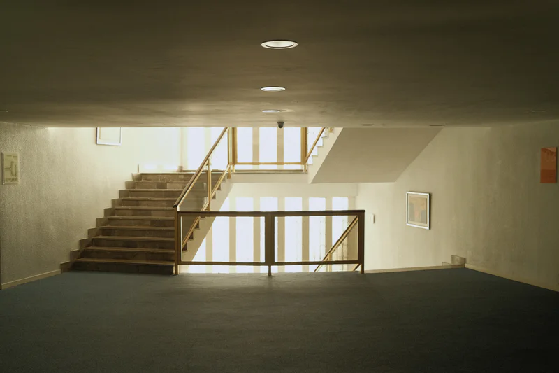 Empty room with dark floor, staircase with handrails, and striped glass panels above.
