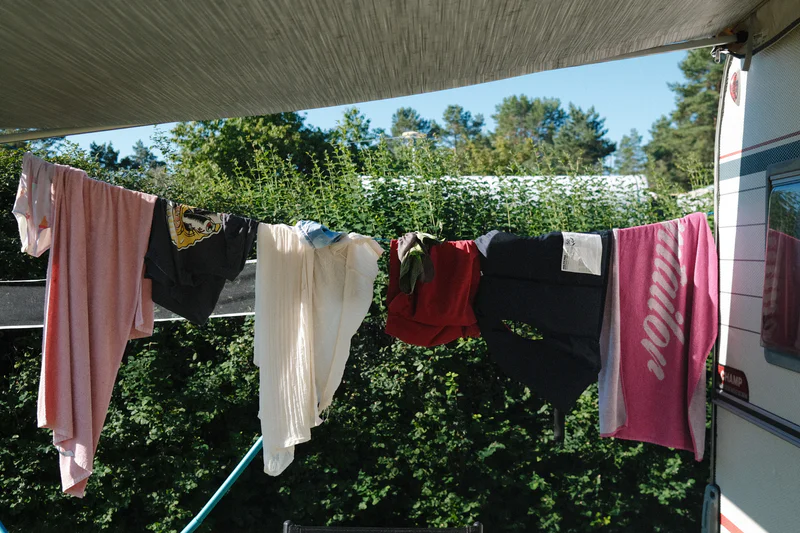 Clothes hang on a line outdoors, with trees and a caravan at the right.