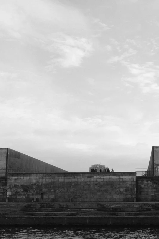 Wide view of concrete buildings and steps by a river under a cloudy sky.