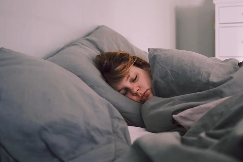 Person asleep on a bed, resting on a gray pillow under a gray comforter.
