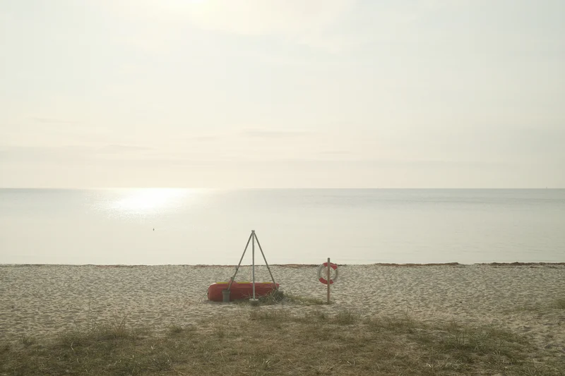 Small lifebuoy station with red buoy on the shoreline near the ocean at dusk.