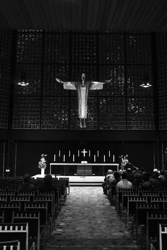 Church aisle leading to a cross and an elevated altar with candles and flowers under dark walls.