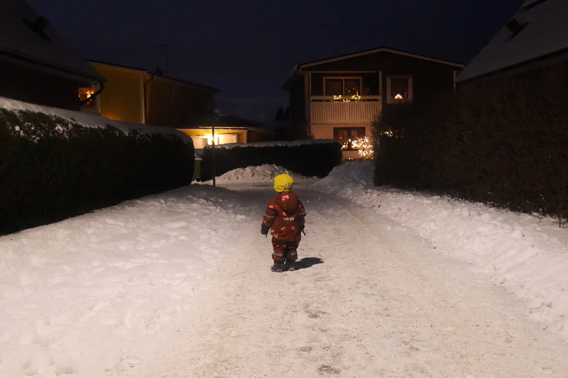 Snowy path at night with a person in winter gear walking toward lit houses.