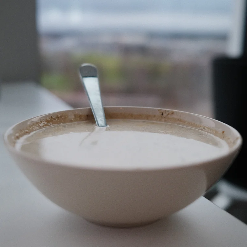 Close-up of a white bowl of creamy soup on a table with a metal spoon standing upright.