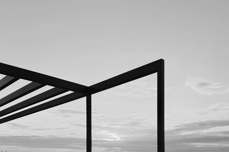 Black metal frame with diagonal beams against a cloudy sky.