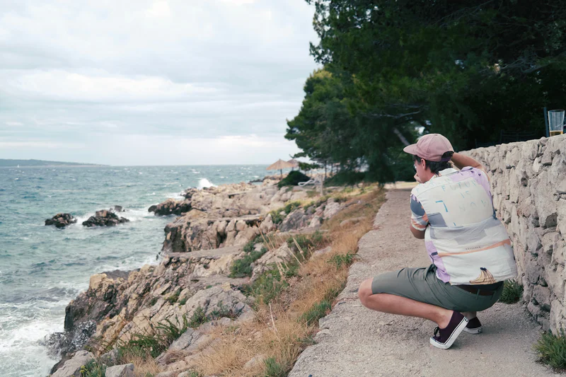A person crouches on a rocky coastal path facing the ocean.