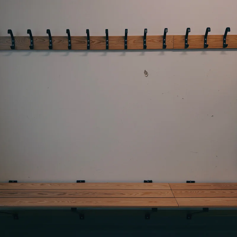 Wood locker bench with a row of dark hooks on the wall above it.