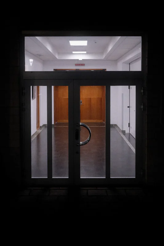 View through a doorway into a hallway with gray walls, wooden doors, and a central metal handle.