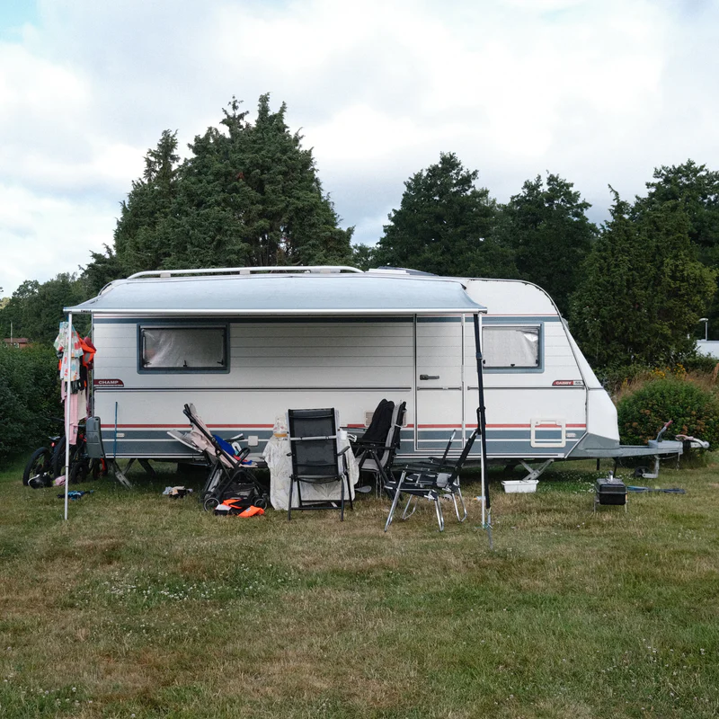 White caravan with windows and awning, camping chairs and equipment on grass.