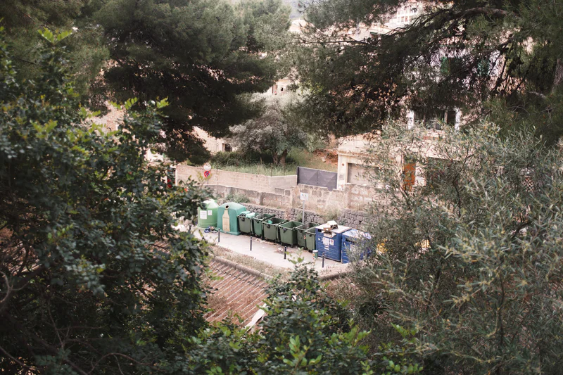 Water treatment area with stone walls, green bins, blue containers, and tracks surrounded by dense trees on a hillside.
