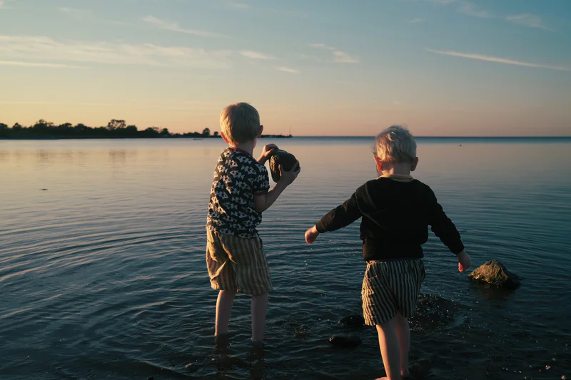 Two children splash in a calm lake at sunset, with their backs to the camera.